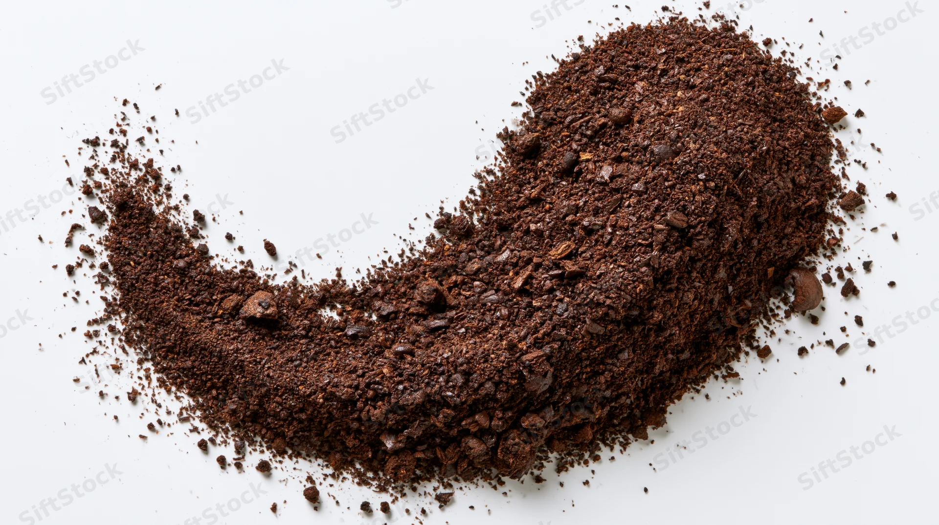 Ground coffee and coarse bean fragments arranged in a curved pile on white background