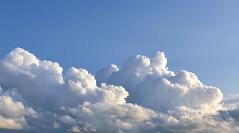 Large billowing cumulus clouds along the lower third of a clear blue sky