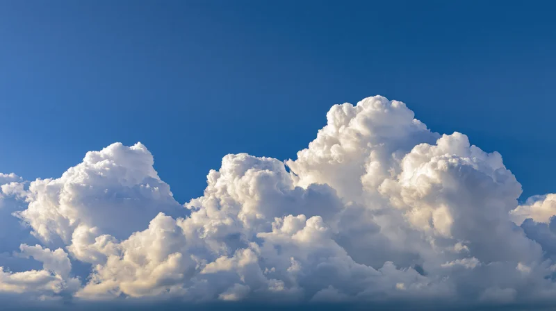 Large billowing cumulus clouds along the lower third of a clear blue sky