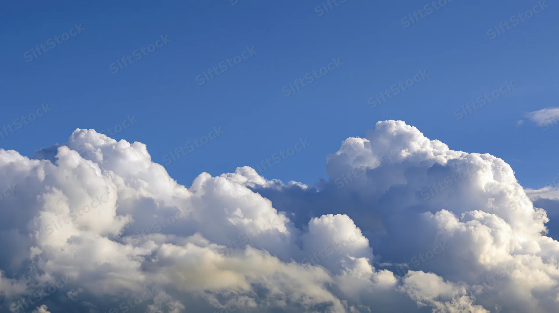 Large billowing cumulus clouds along the lower third of a clear blue sky