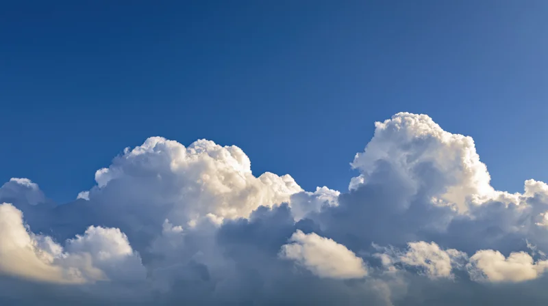 Large billowing cumulus clouds along the lower third of a clear blue sky