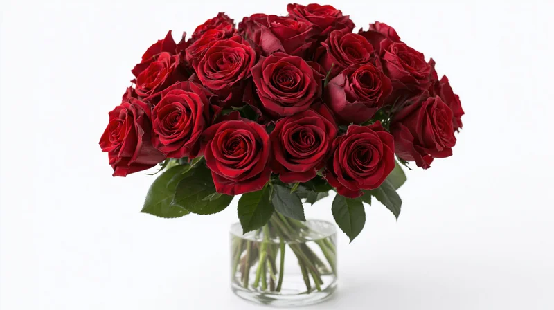 Large bouquet of deep red roses arranged densely in a clear glass vase on white background