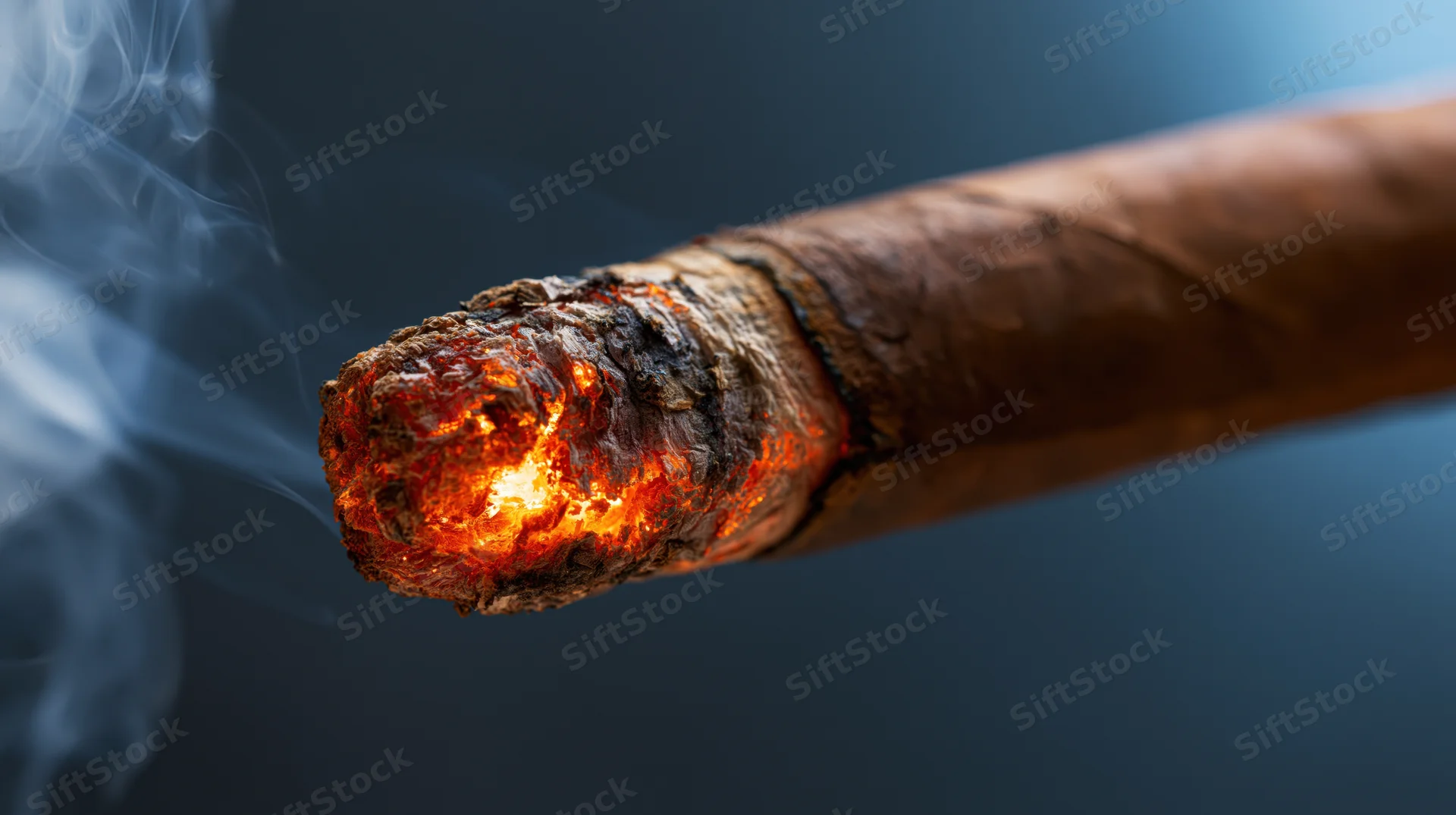 Close-up of a lit cigar tip burning with glowing orange ember and rising smoke against a dark blue background