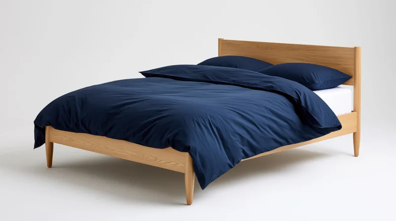 Minimalist wooden double bed with navy bedding and white mattress on plain white background