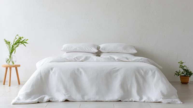 Neatly made white bed with pillows and linen bedding in minimalist bedroom interior
