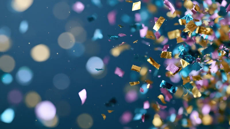 Multicolored metallic confetti and foil streamers falling against a blue bokeh background