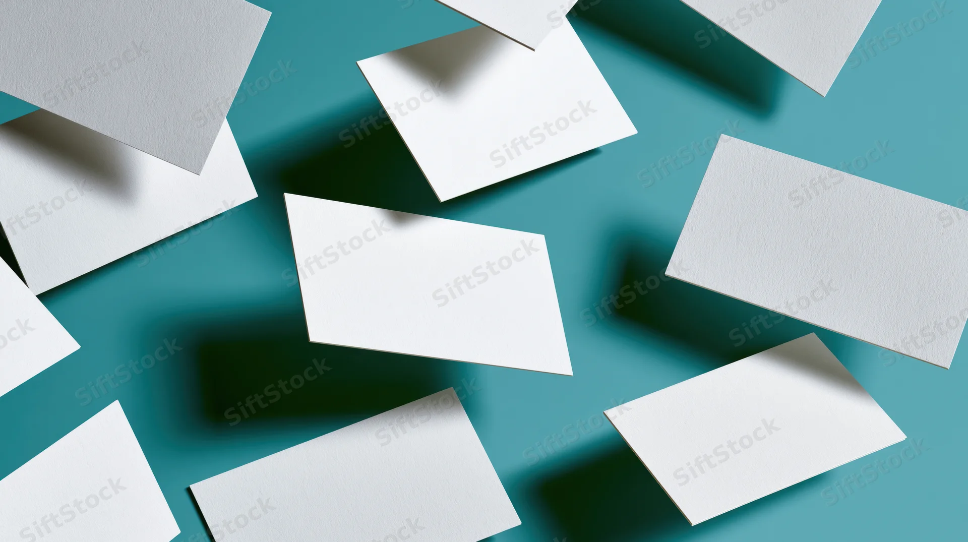 Blank white business cards tumbling and scattered on a teal background