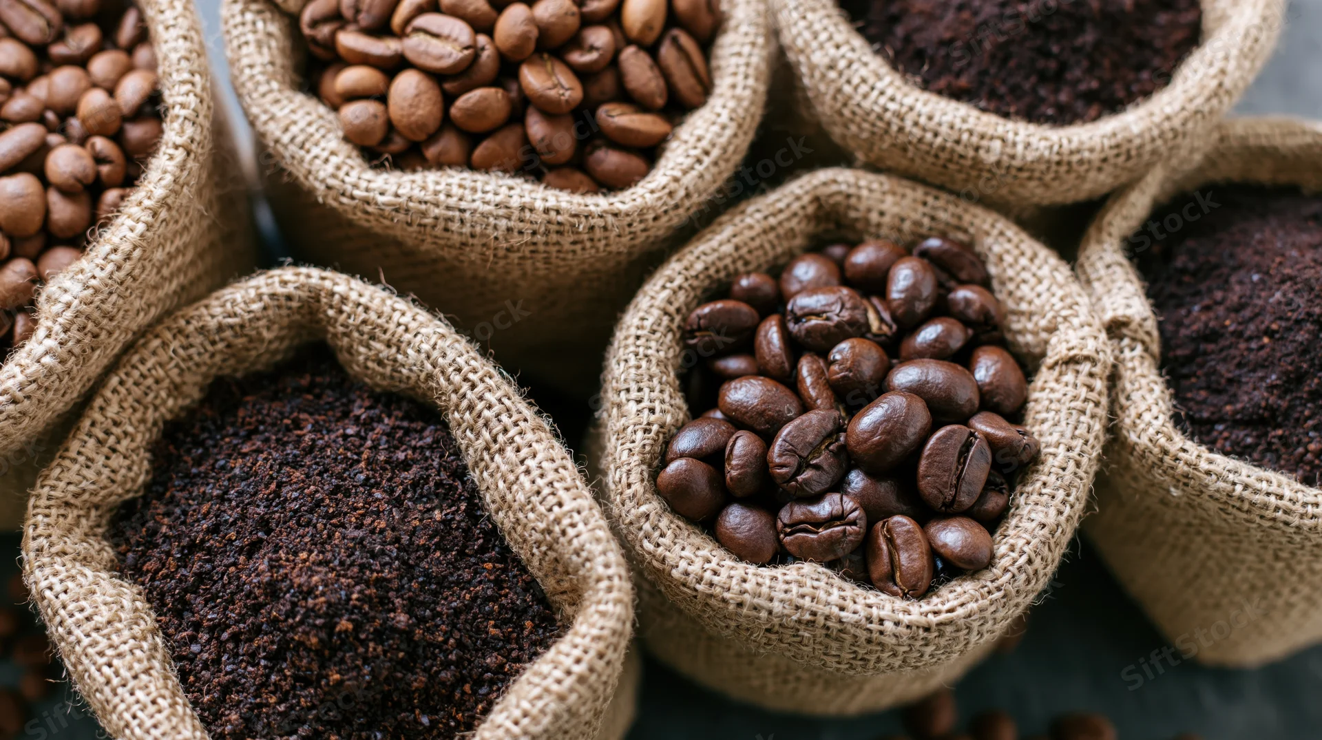 Roasted coffee beans and ground coffee in small burlap sacks arranged closely together