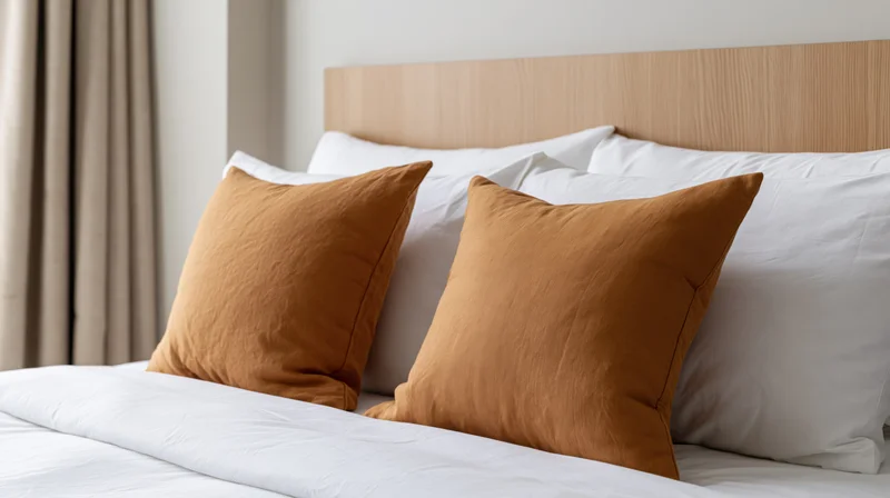 Neatly made hotel bed with white and amber-ochre pillows against a wooden headboard