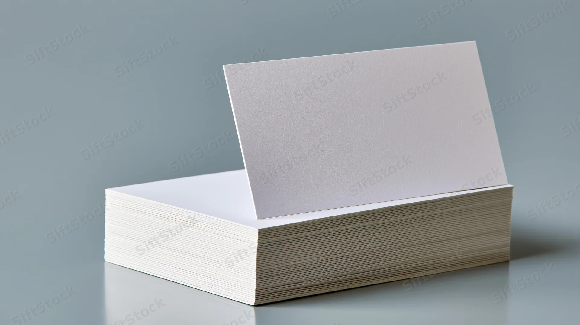 Blank white business card standing upright against a stack of cards on a gray surface