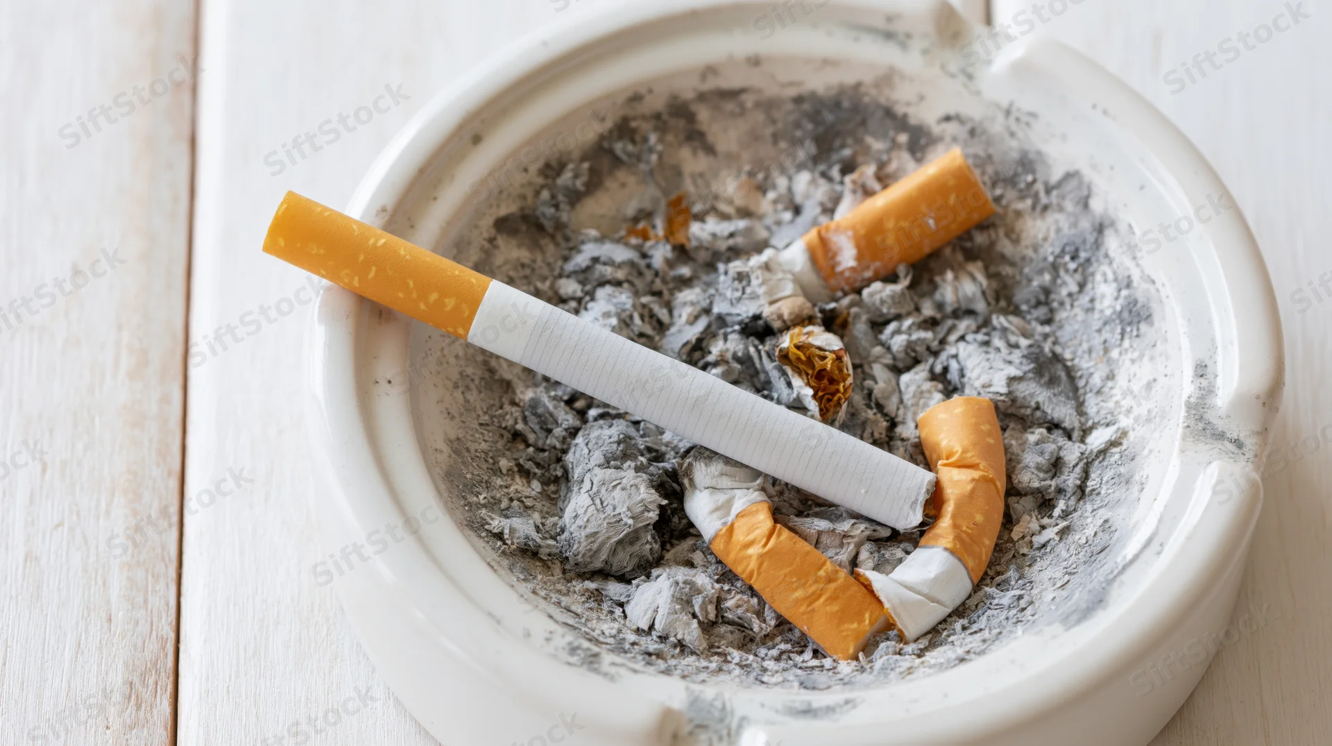 Unlit cigarette resting diagonally across a full ashtray on a wooden table