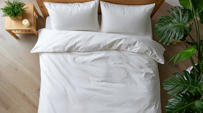 Overhead view of a neatly made double bed with white bedding and green plants in a modern bedroom