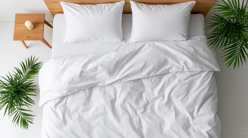 Overhead view of a neatly made double bed with white bedding and green plants beside it