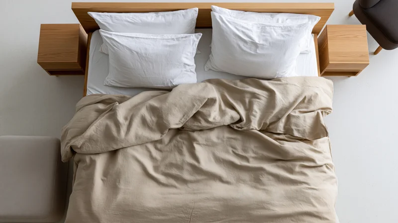 Overhead view of a double bed with white pillows and beige comforter in a minimalist bedroom