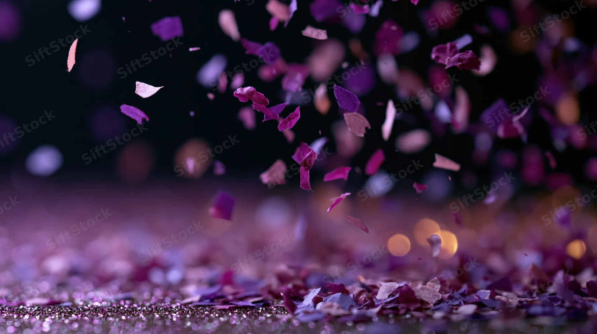 Purple and pink confetti pieces falling and scattering midair over a glittery surface in low light