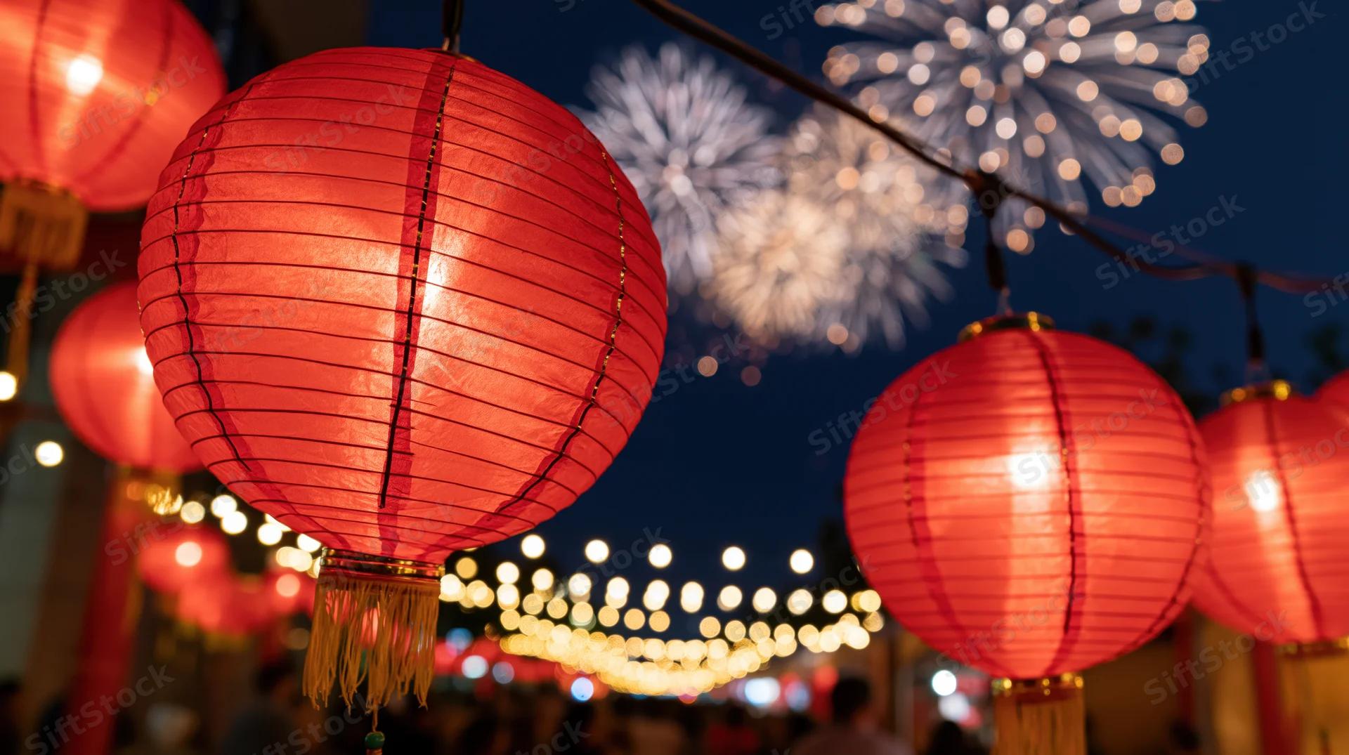 Red chinese paper lanterns glowing in the night with fireworks in the background