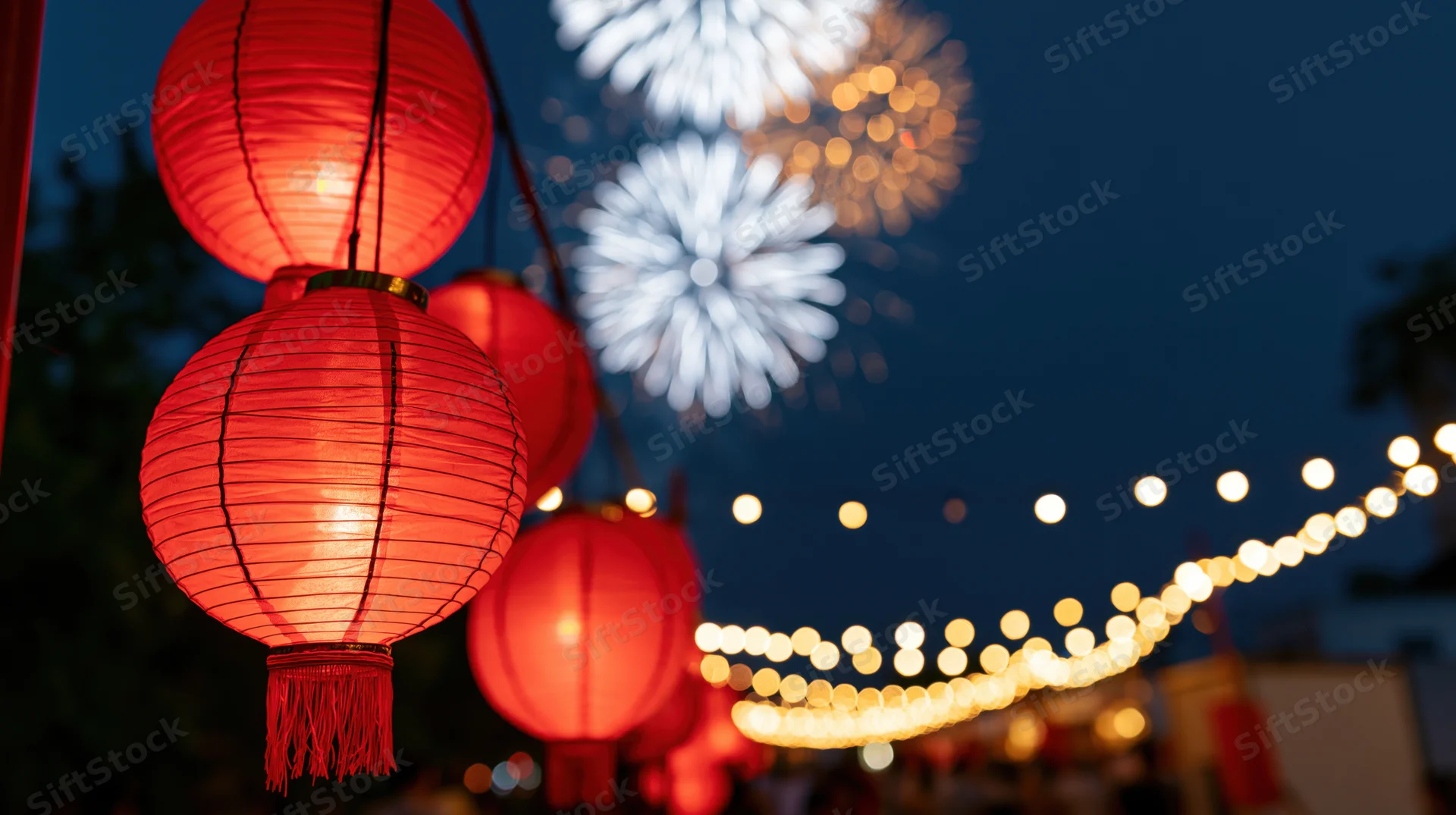 Red chinese paper lanterns glowing in the night sky with fireworks and string lights in the background