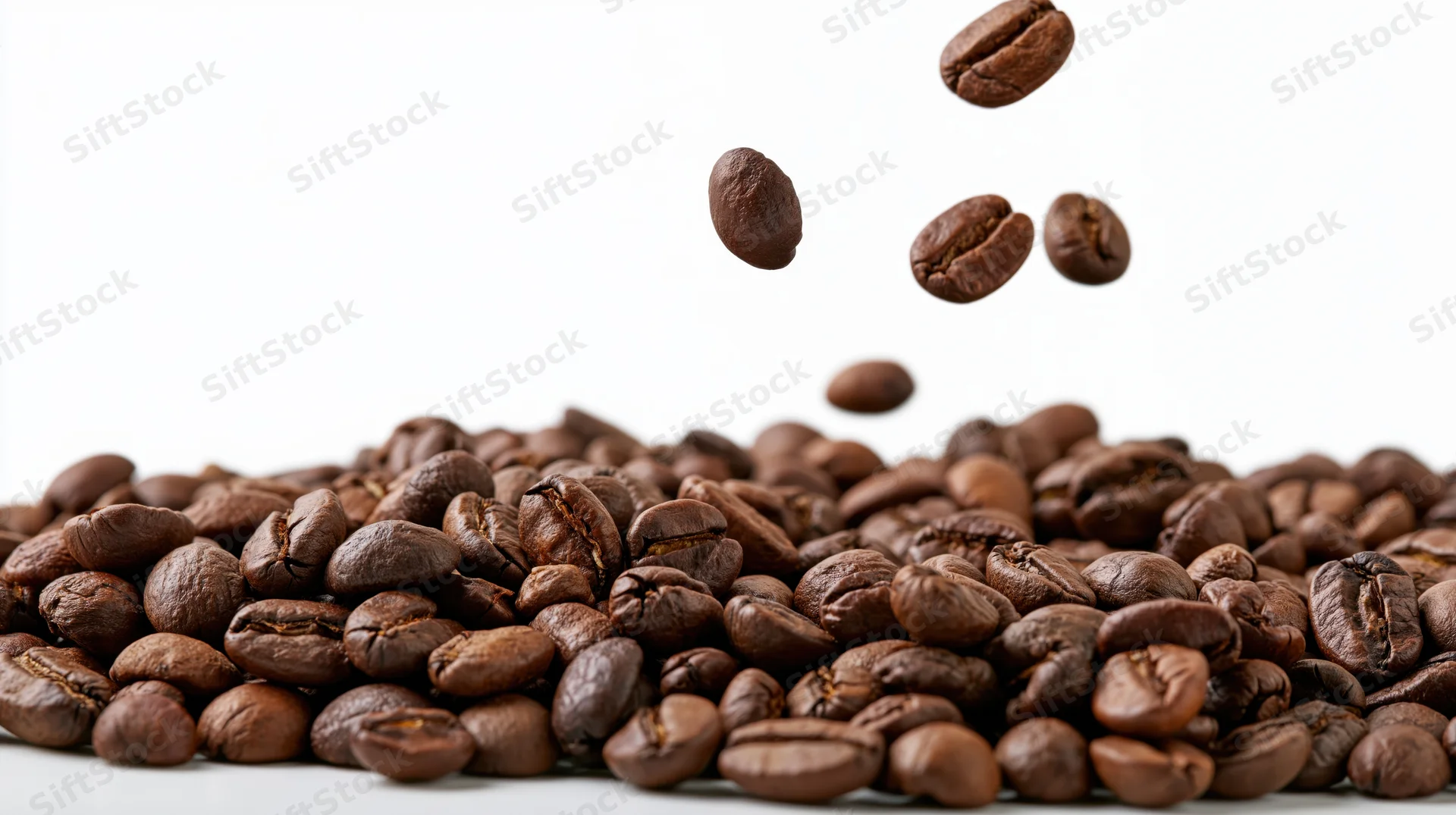 Roasted coffee beans falling midair onto a pile against a white background
