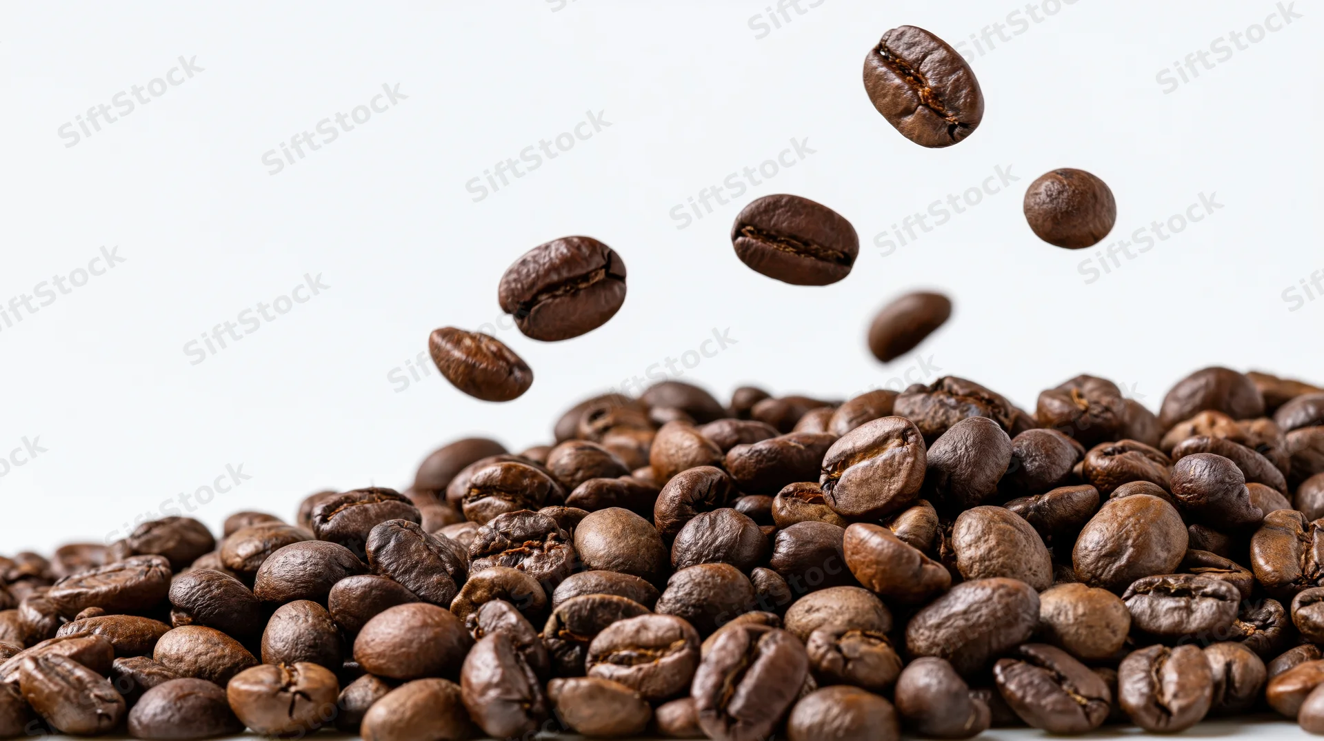 Roasted coffee beans falling midair over a pile against white background