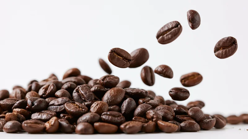 Roasted coffee beans falling midair onto a pile against a white background