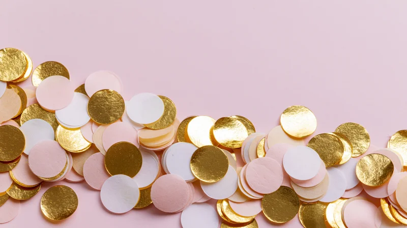 Scattered round confetti pieces in gold, white and pale pink on a pink surface