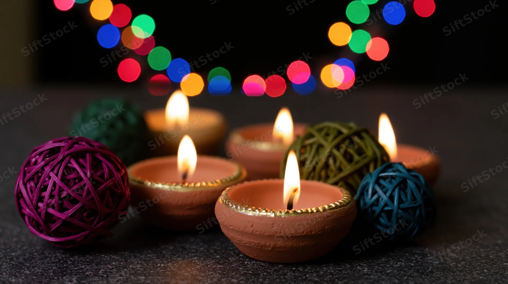 Lit clay diya oil lamps arranged on dark surface with colorful bokeh lights in background