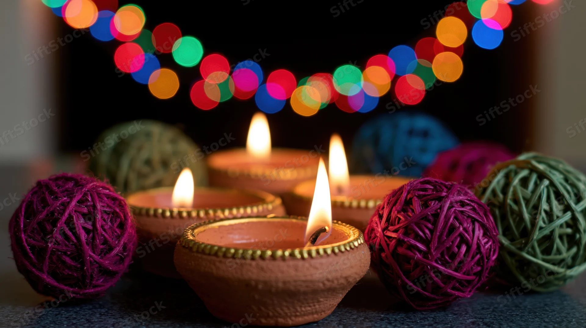 Lit clay diya oil lamps arranged on dark surface with colorful string lights in background