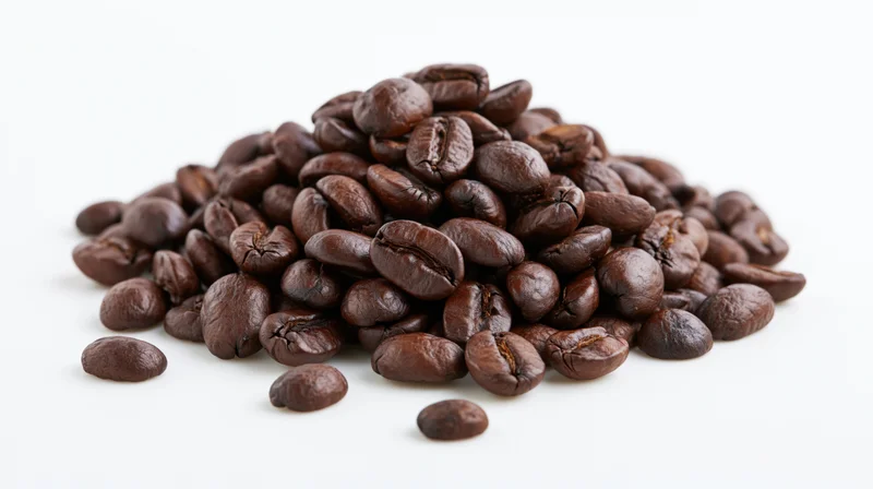 Pile of dark roasted coffee beans scattered on white surface