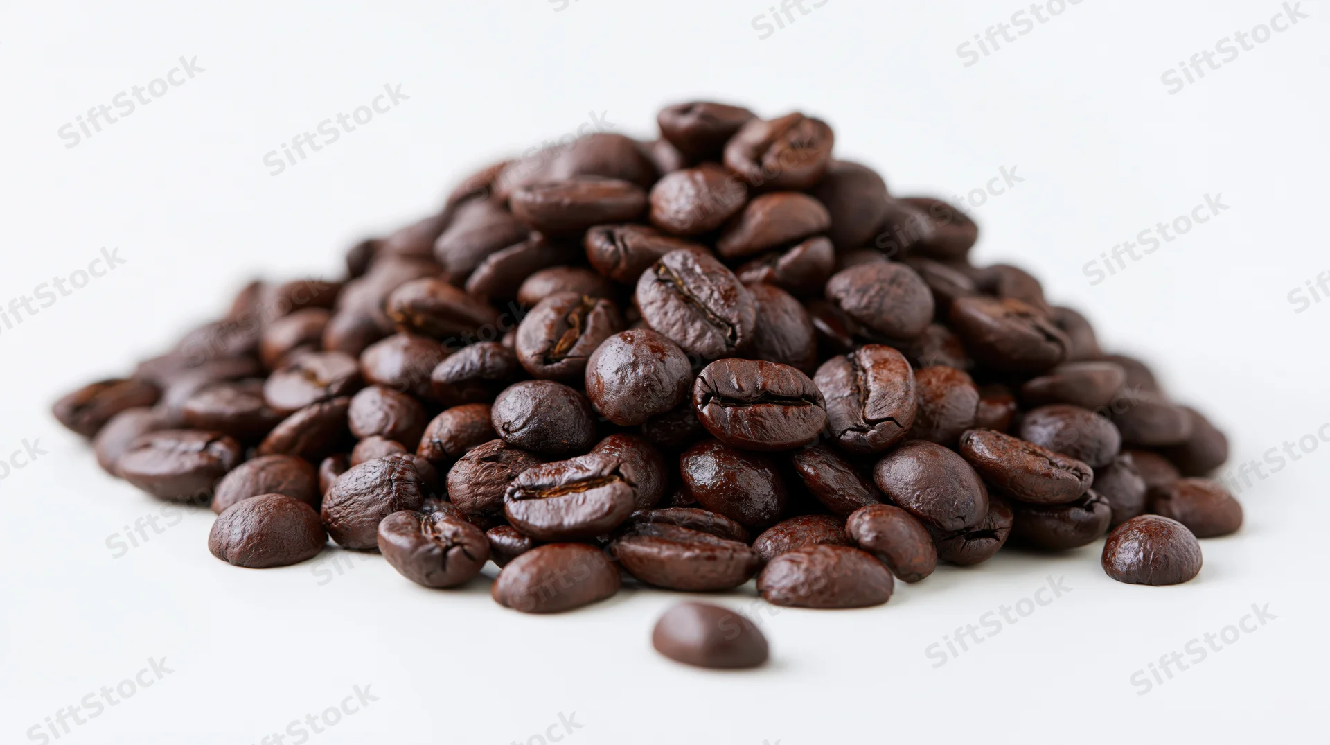 Pile of dark-roasted coffee beans scattered on white surface