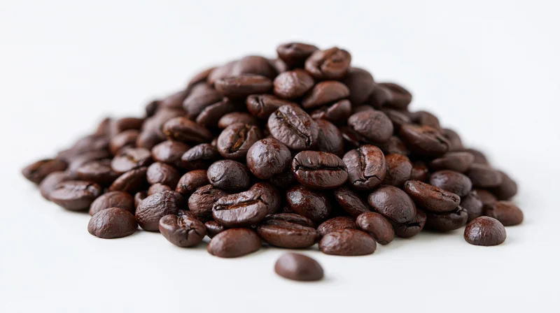 Pile of dark-roasted coffee beans scattered on white surface