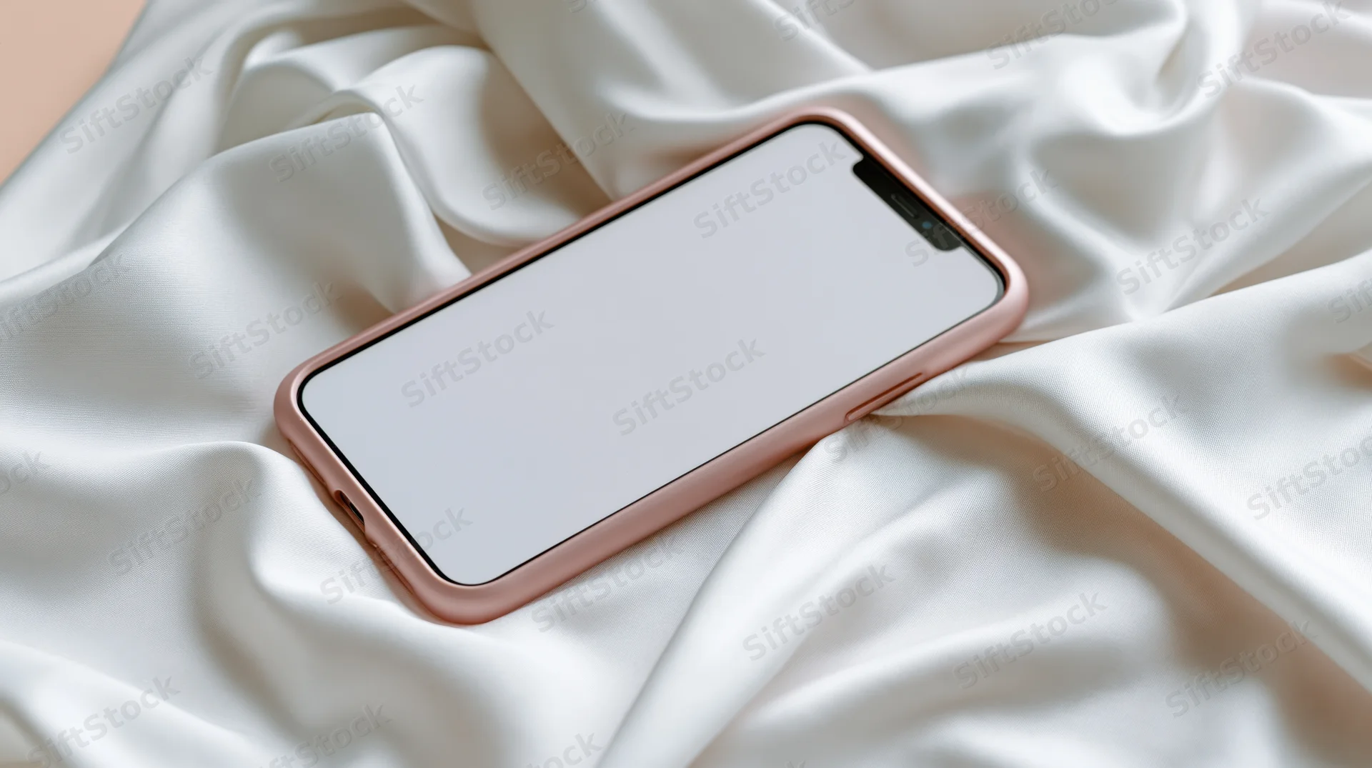 Smartphone with rose gold case lying on white silk fabric