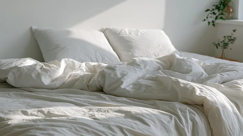 Unmade bed with rumpled white bedding and two pillows in a bright bedroom