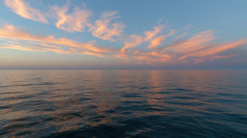 Vast open ocean at dusk with wispy clouds reflecting in calm water