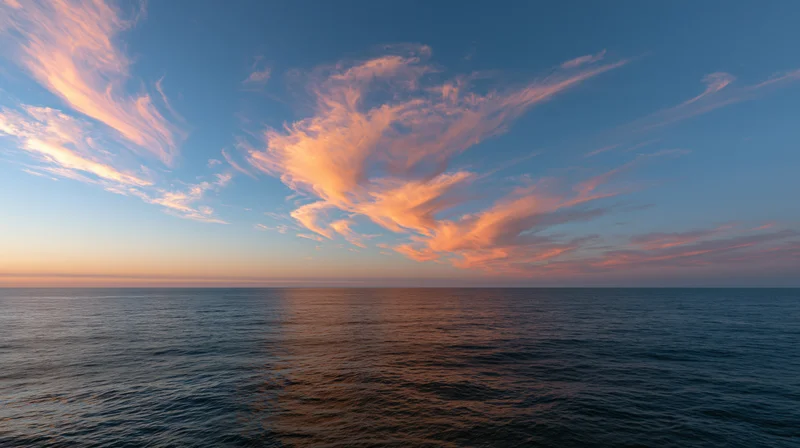 Vast open ocean at dusk with wispy clouds lit by sunset reflecting on calm water