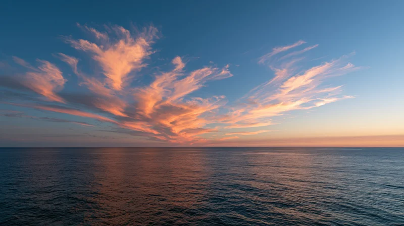 Vast ocean at dusk with wispy clouds lit by sunset reflecting on calm water