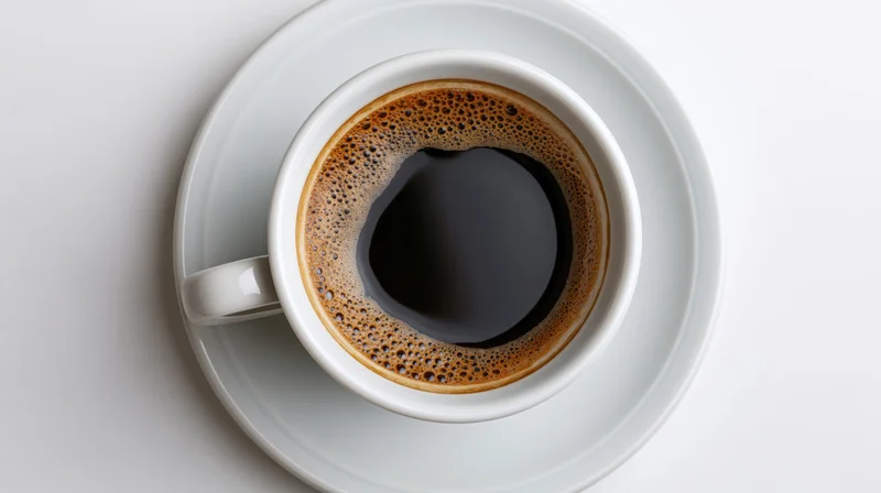 White ceramic coffee cup filled with black coffee on saucer viewed from above