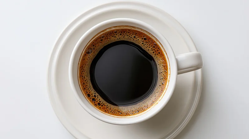 White ceramic coffee cup filled with black coffee on saucer viewed from above on plain surface
