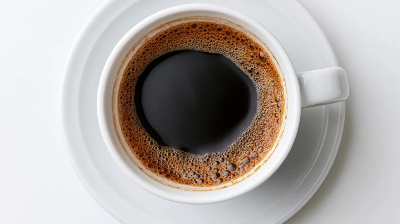 White ceramic coffee cup filled with black coffee on saucer viewed from above