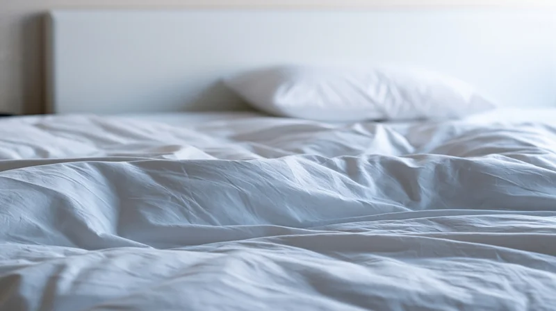 White hotel bed with rumpled cotton duvet and pillow resting