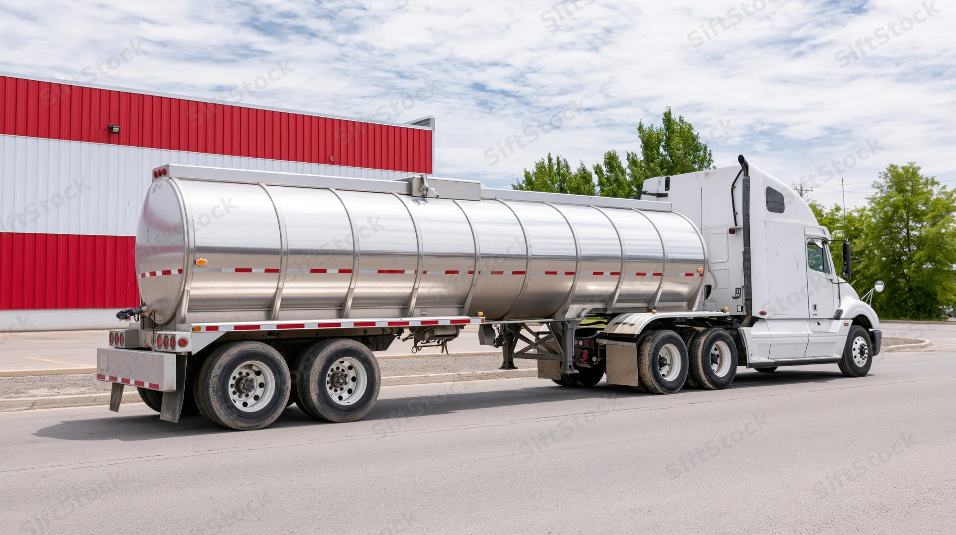 White semi-truck with polished stainless steel tanker trailer parked in front of red and white building