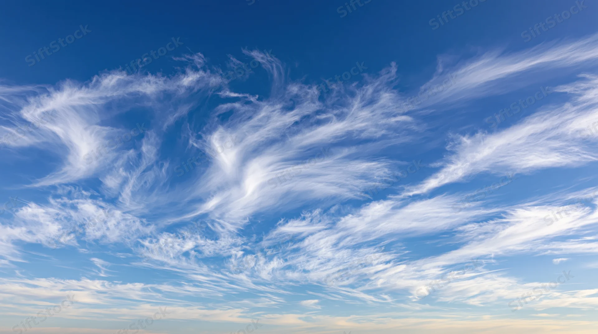 Wide upward view of open daytime sky filled with wispy white clouds against deep blue background