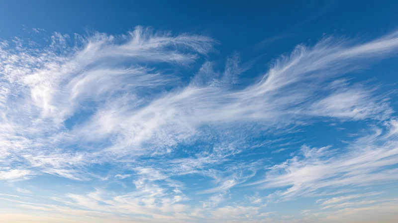 Wispy white clouds drifting across a clear blue sky during daytime