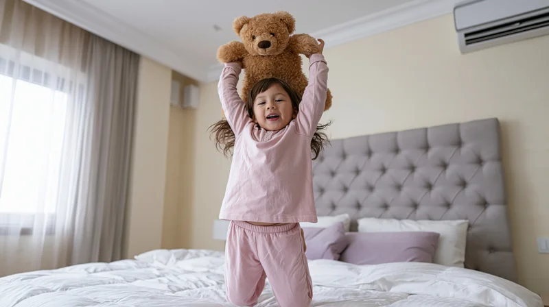 Young girl in pink pajamas jumping on bed with teddy bear on head