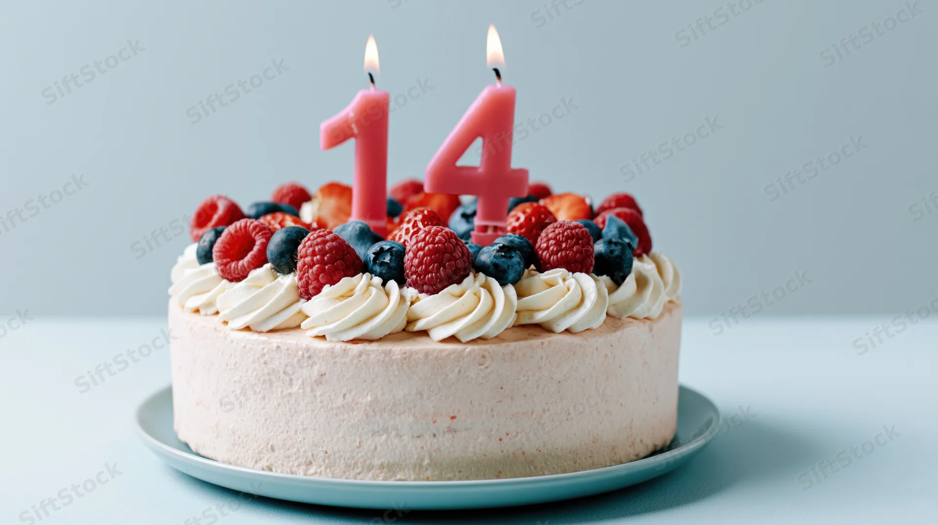 Birthday cake with lit number 14 candles and berries on cream frosting on a plate