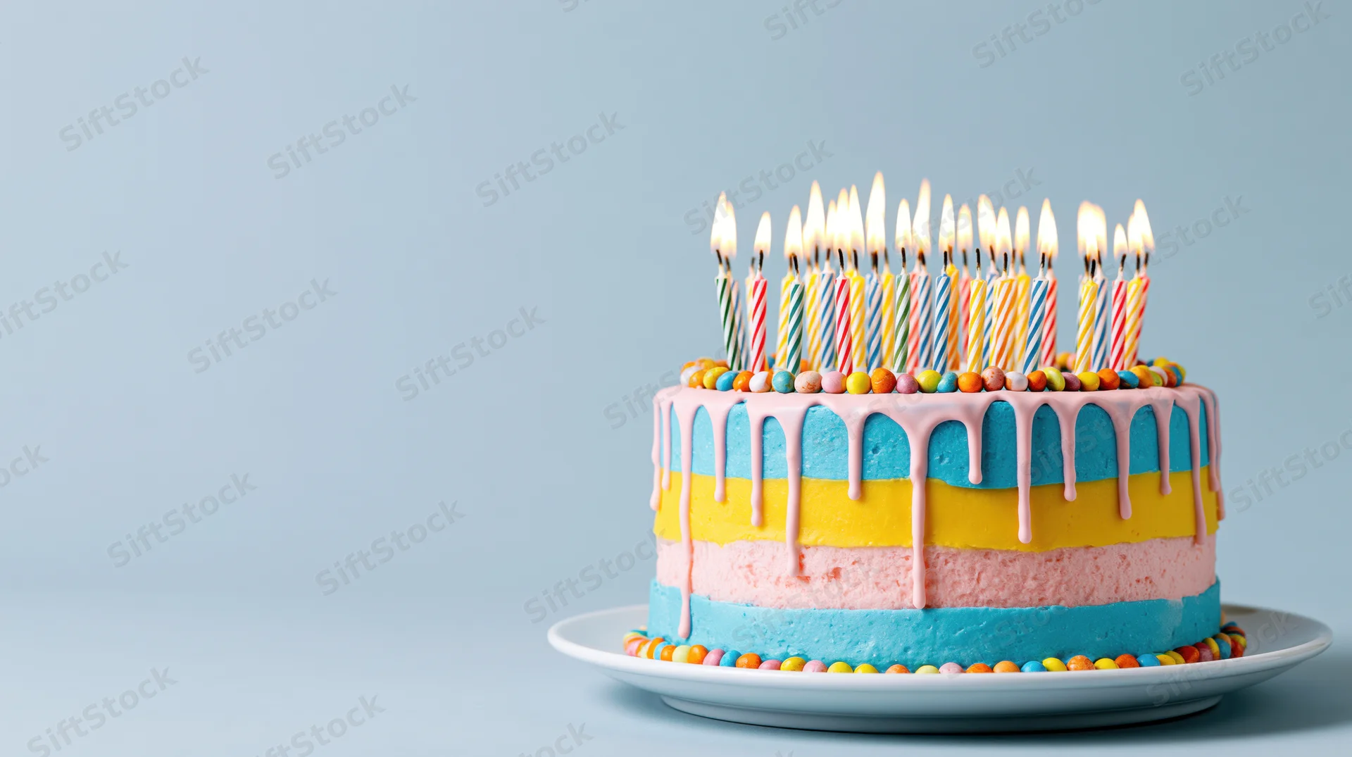 Colorful birthday cake with lit candles on a white plate against a light blue background