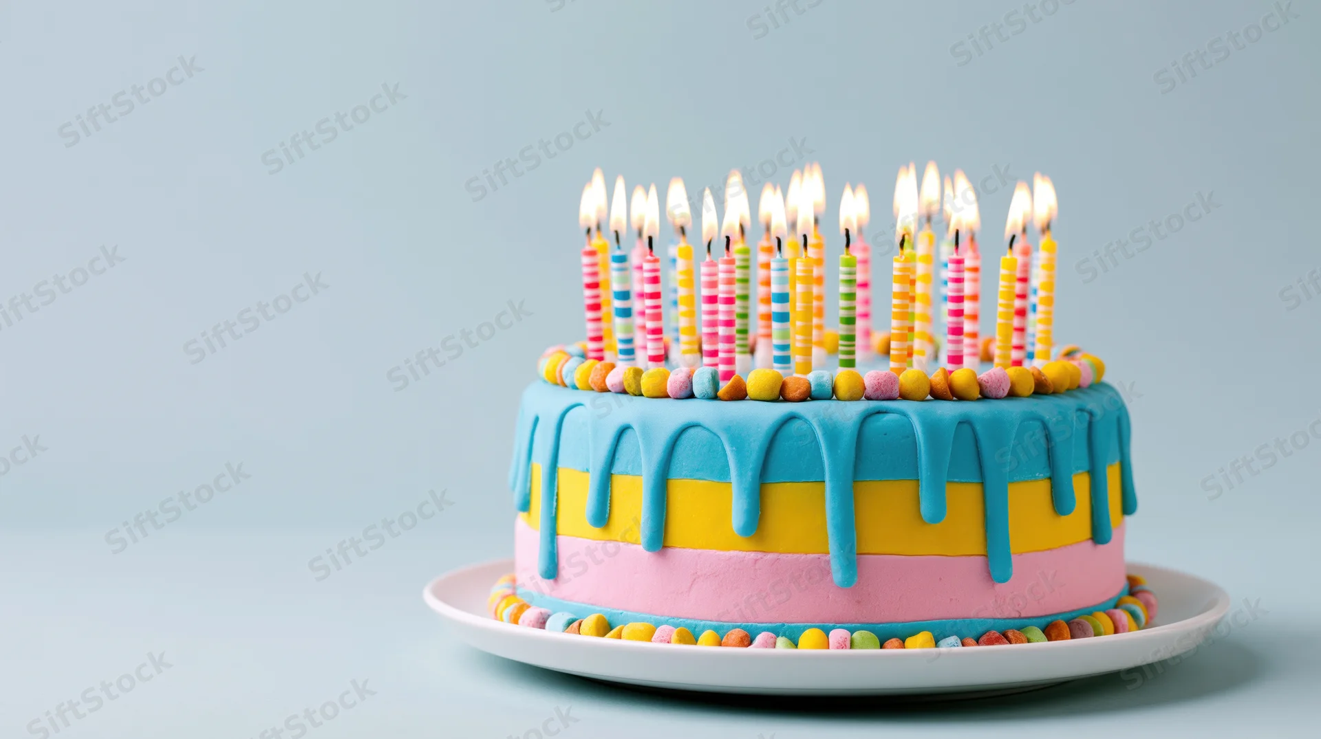 Colorful birthday cake with lit candles on a white plate against a light blue background