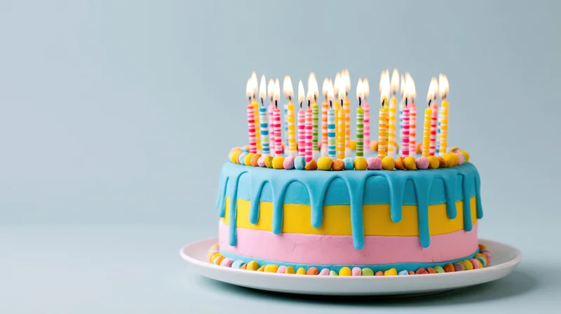 Colorful birthday cake with lit candles on a white plate against a light blue background