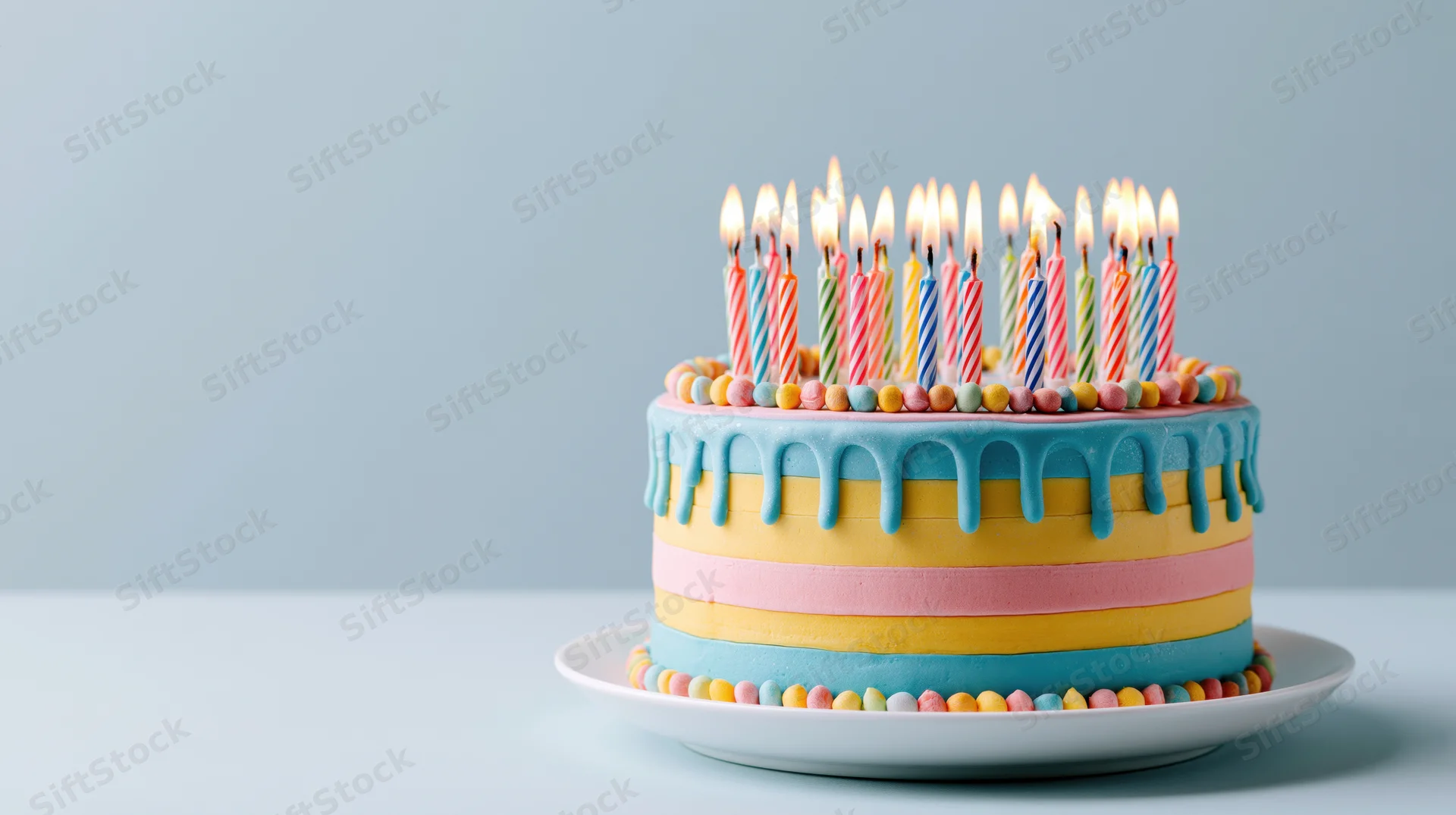 Colorful birthday cake with lit candles on a white plate against a light blue background