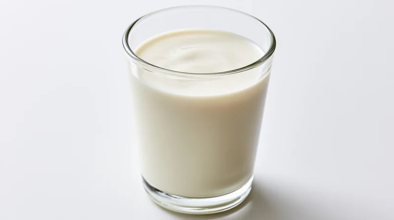 A clear glass filled with white milk on a plain white surface