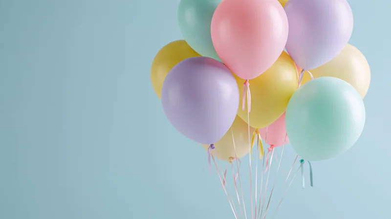 Cluster of pastel-colored helium balloons floating against a light blue background with copyspace